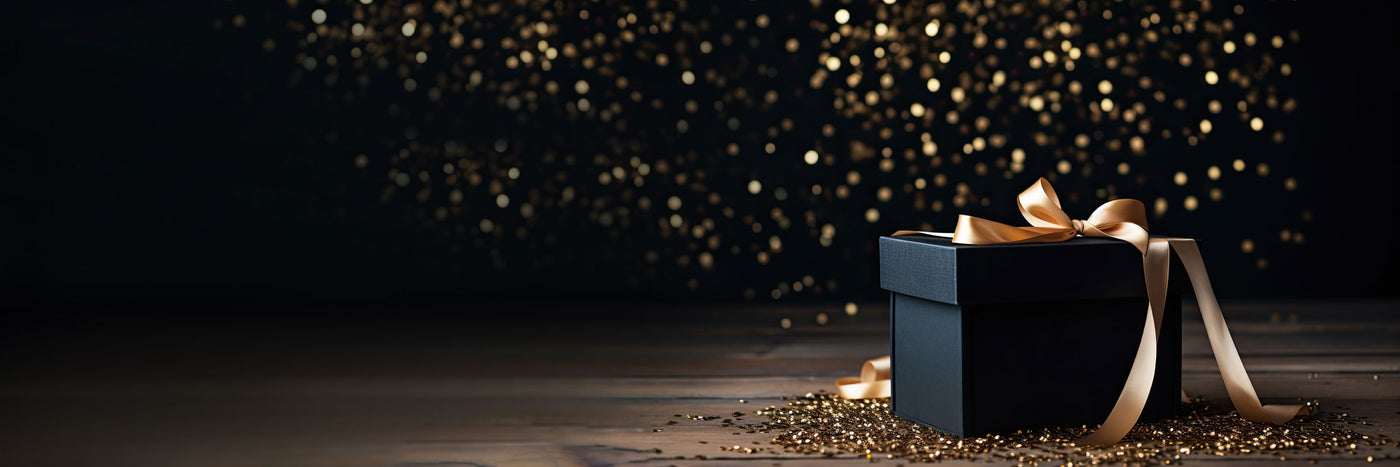 Black gift box with gold ribbon on a wooden surface with a dark, starry background