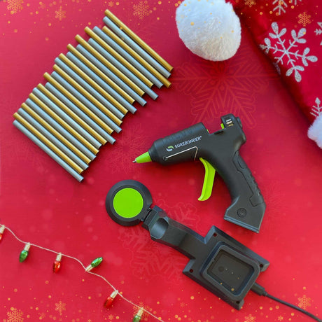 Hot glue gun and accessories on a red background with Christmas decorations.